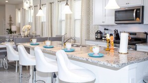 A modern kitchen with white cabinetry, a large island with bar stools, a microwave, and a gas stove. - BR Villa w/ Pool, Star Wars Game Room + Resort (Davenport)