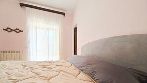 A bedroom with a bed, a radiator, a window with sheer curtains, and a door. - Anna Cerasuolo House | Whole house in mountain hamlet (Molise)