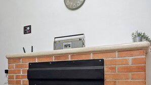 A brick fireplace with a black glass door, a clock above it, and a small radio on the mantel. - Anna Cerasuolo House | Whole house in mountain hamlet (Molise)