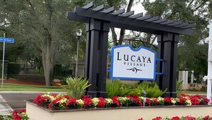Un panneau indiquant l’entrée du village de Lucaya, avec une structure en forme de pergola et des parterres de fleurs.