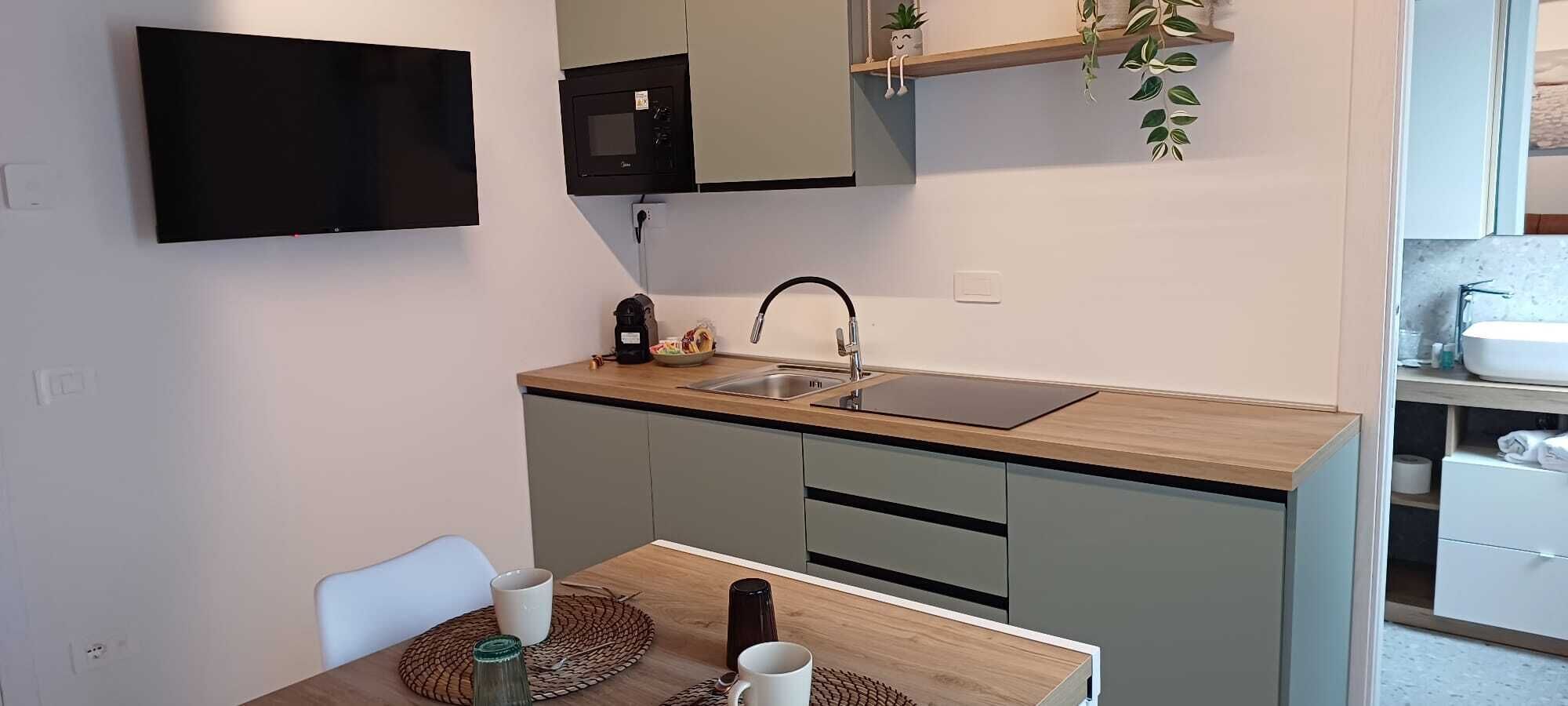 A compact kitchen with a flat-screen TV, a microwave, a sink, and a small dining area with a table and chairs.