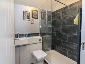 Ein modernes Badezimmer mit einer gläsernen Duschkabine, einer weißen Toilette und einem Waschtisch mit Spiegel und gerahmten Bildern.