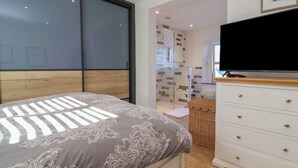 Un dormitorio con cama, televisor, cómoda y zona de ducha.