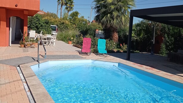 A swimming pool with a tiled edge, surrounded by a patio area with chairs and a covered seating area.