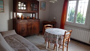 A cozy room with a wooden cabinet, a dining table with chairs, a sofa, and a window with curtains.