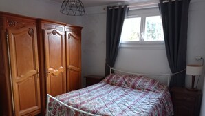 A bedroom with a bed, wooden wardrobe, and a window with curtains.
