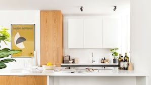 A modern kitchen with a white countertop, wooden cabinets, and black bar stools. - The Marlo (London)