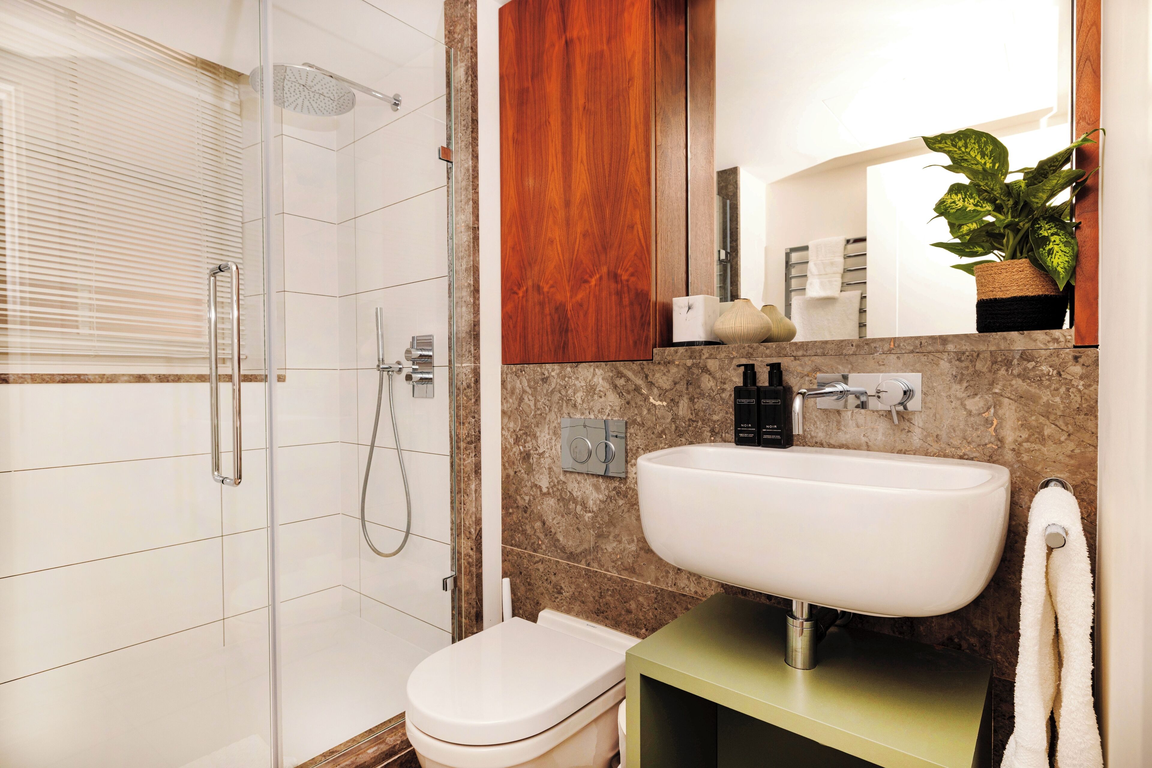 A modern bathroom with a glass-enclosed shower, a white toilet, and a sink with a marble countertop.