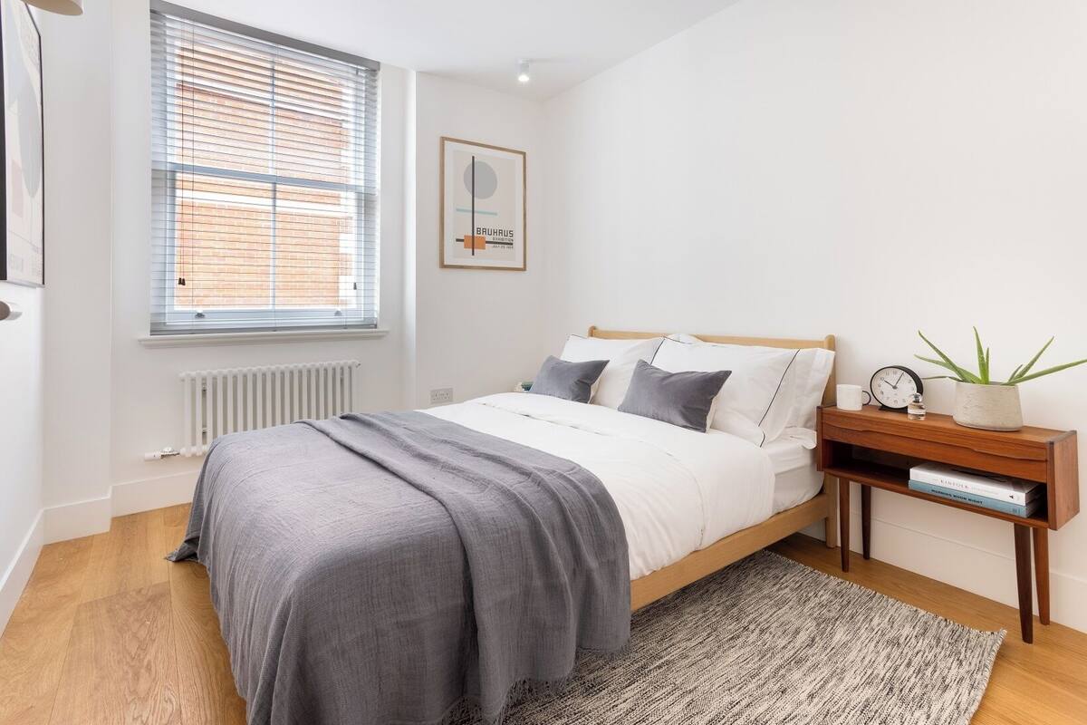 A modern bedroom with a bed, bedside table, and a window with blinds.