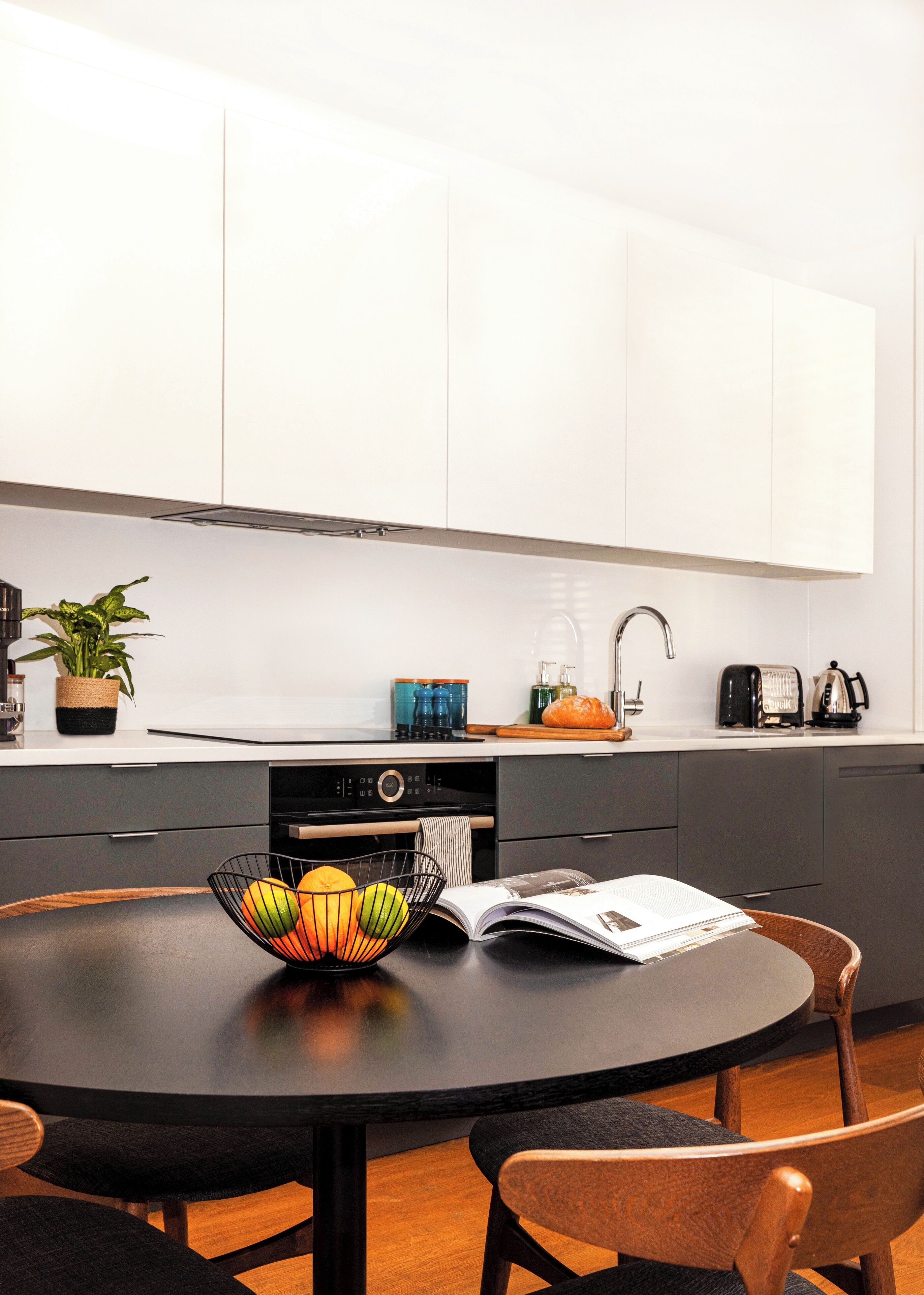 A modern kitchen with white cabinets, a black countertop, a round dining table, and a few chairs.
