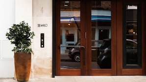 A hotel entrance with a large potted plant, a digital keypad, and a glass door reflecting a car and a building across the street. - The Marlo (London)