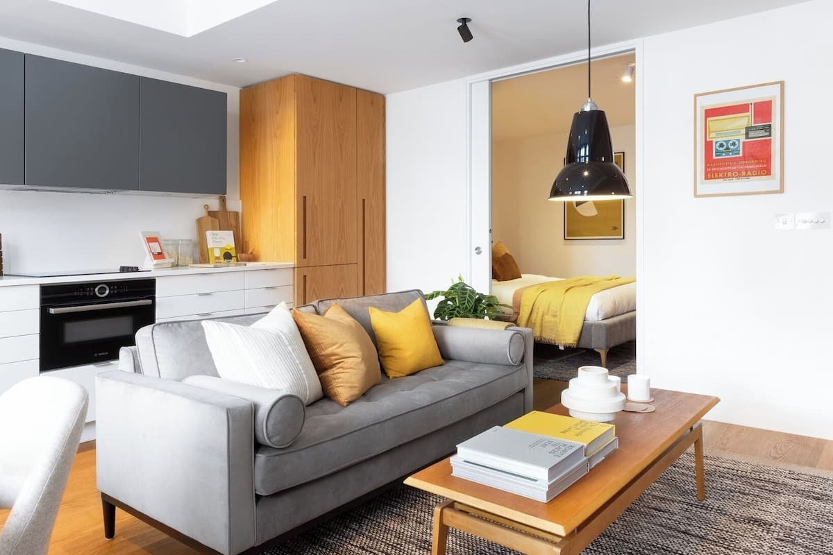 A modern living room with a grey sofa, a wooden coffee table, and a kitchen area with grey cabinets and a Bosch oven.