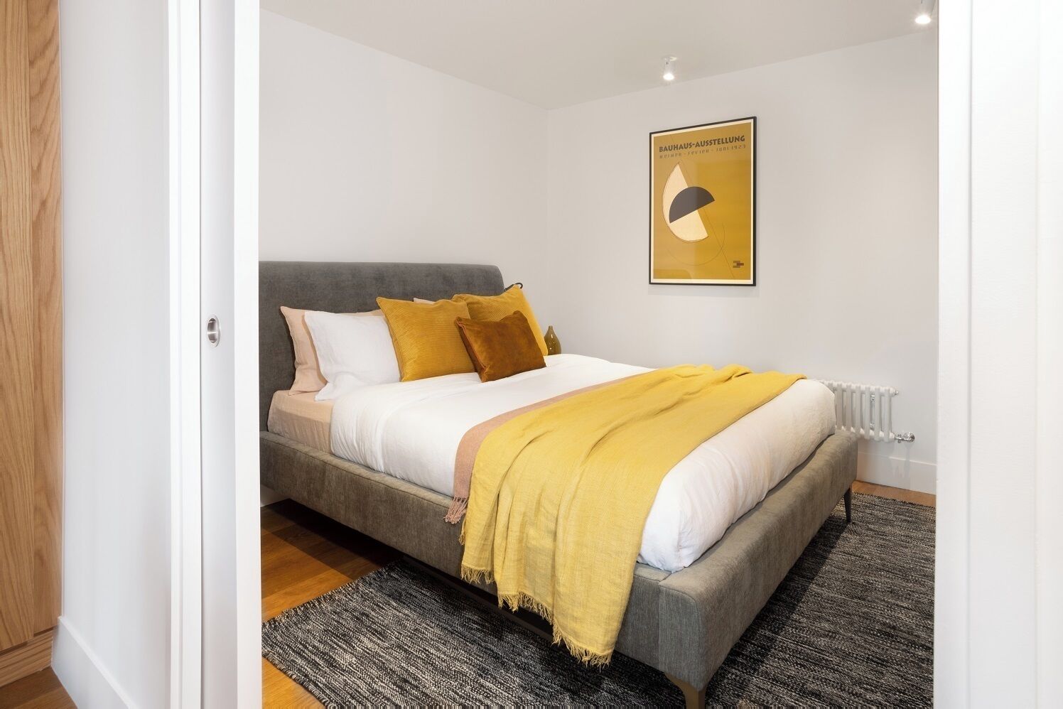 Ein Schlafzimmer mit Bett, Kissen, Decke, Heizkörper und einem Bild an der Wand.