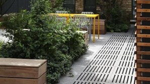 A courtyard with a wooden bench, a yellow table, and a planter. - The Marlo (London)