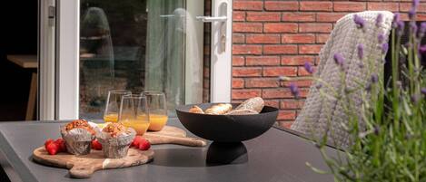 A breakfast setup with muffins, strawberries, and orange juice on a table outside a room with a brick wall and a sliding glass door.