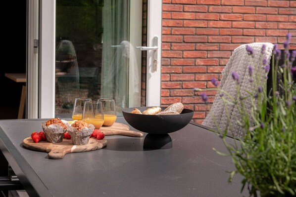 A breakfast setup with muffins, strawberries, and orange juice on a table outside a room with a brick wall and a sliding glass door.
