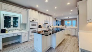 A modern kitchen with white cabinetry, a central island, and recessed ceiling lights. - The Channel House~Water Views~Dock + Boatslip~Walk to beach! (Wrightsville Beach)