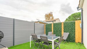 Een terras met een tafel, stoelen, een barbecue en een groene wand met begroeiing.