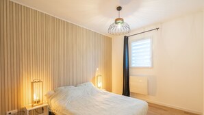 Een slaapkamer met een bed, nachtlampjes, een raam met gordijnen en een lambrisering.