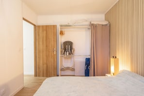 Une chambre à coucher comprenant un lit, une armoire en bois, un placard avec une tringle, et une table de chevet avec une lampe.