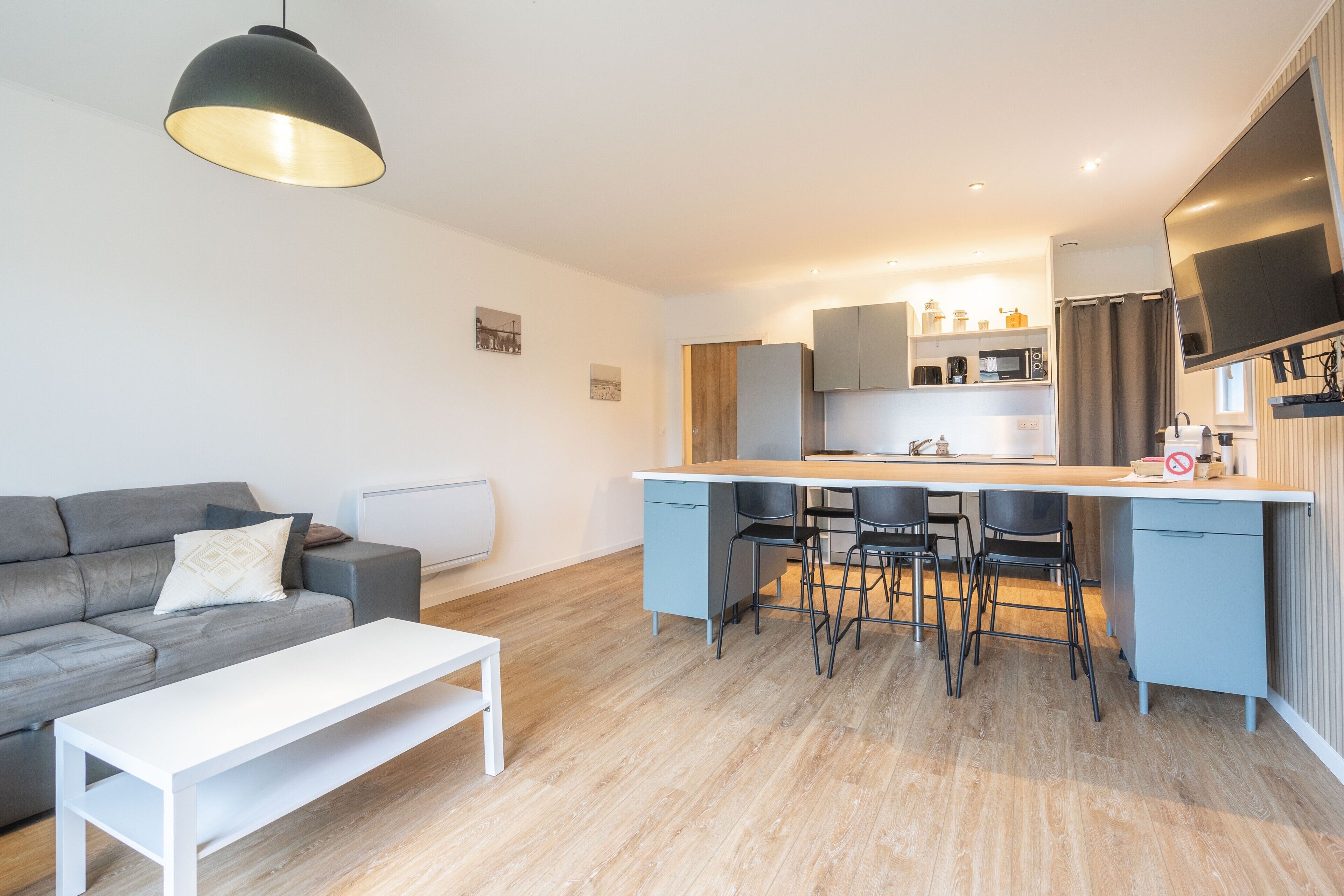 A modern kitchen with a central island, bar stools, and a flat-screen TV.