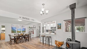 A modern kitchen with white cabinets, a central island, bar stools, and a wood-burning stove. - 25 min to Yosemite - BBQ - Hot Tub -  Private Creek (Oakhurst)