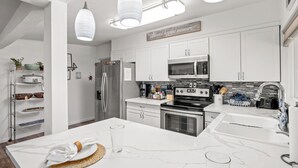 A modern kitchen with white cabinetry, stainless steel appliances, and a marble countertop. - 25 min to Yosemite - BBQ - Hot Tub -  Private Creek (Oakhurst)