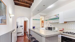A kitchen with a central island, bar stools, a stove, and a refrigerator. - Campo 8 - Spacious Apartment with View of Campo dè Fiori (Roma)