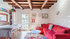 A cozy living room with a red sofa, a small round table, and a dining area with a table set for four. - Campo 8 - Spacious Apartment with View of Campo dè Fiori (Roma)