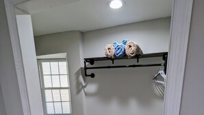 Ein Zimmer mit Holzboden, Deckenleuchte, Fenster mit Jalousien und Handtuchhalter mit Handtüchern.