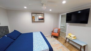 Ein Schlafzimmer mit einem Bett, einem Sessel, einer Bank, einem Fernseher und einem Deckenventilator.
