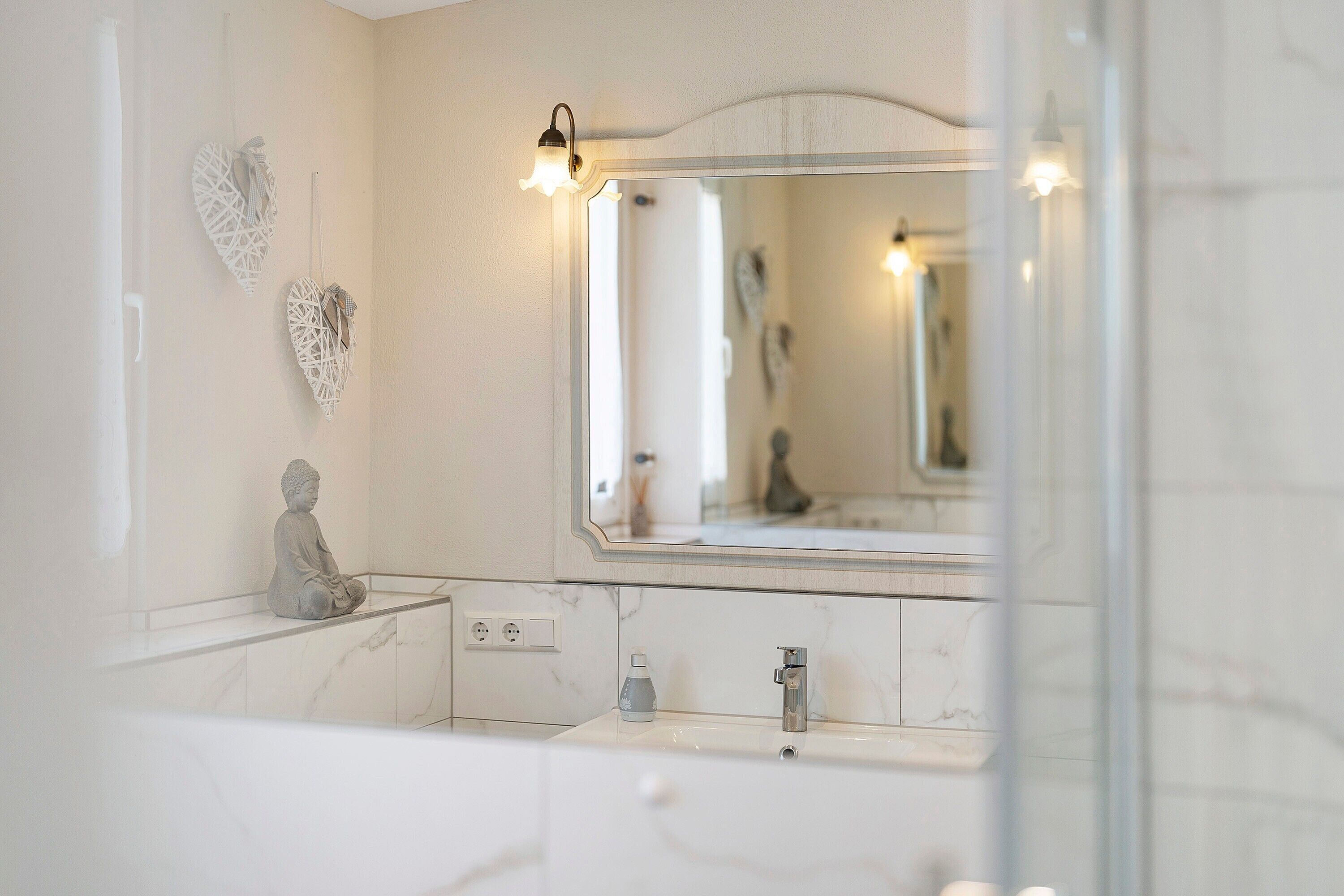 Une salle de bain avec un lavabo en marbre, un miroir et une statue de Bouddha.