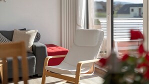 Ett modernt vardagsrum med en grå soffa, en röd pall, en vit fåtölj och en trästol.