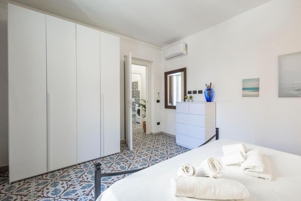 A bedroom with a bed, white wardrobe, and a bathroom visible through an open door.