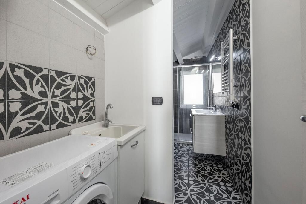 A compact bathroom with a washing machine, a sink, and a mirror.