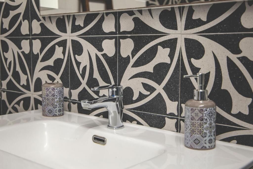 Une salle de bain avec un lavabo blanc, un robinet moderne et deux distributeurs de savon à motifs.