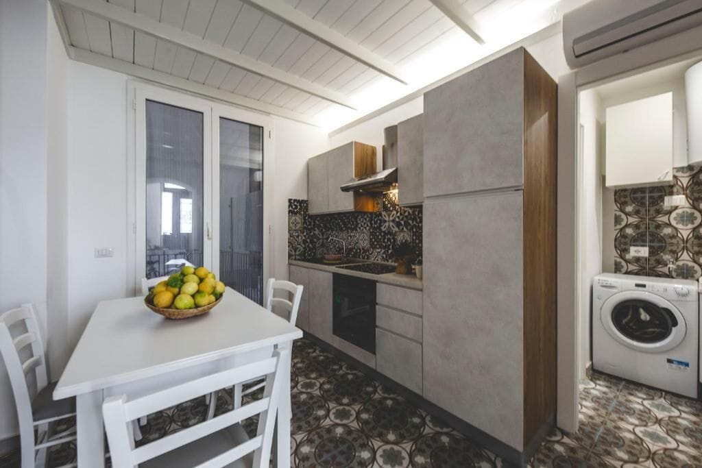 Une cuisine compacte comprenant une table à manger, des chaises, un lave-linge et des carreaux décorés.