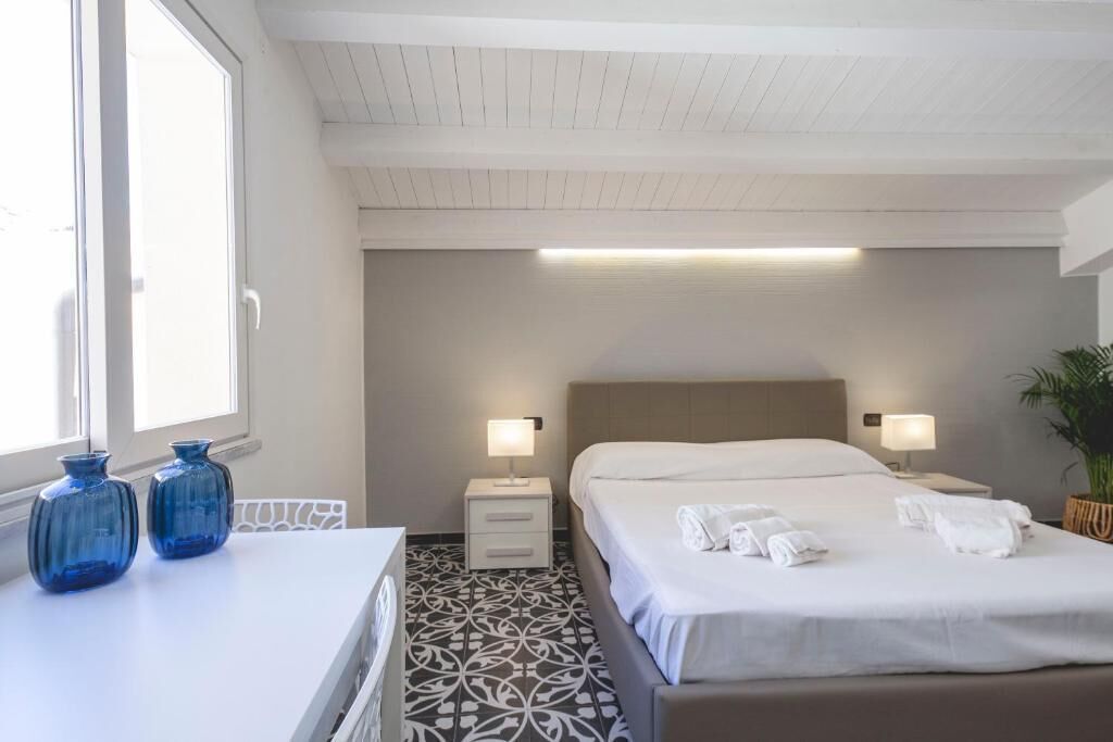 Una habitación de hotel con cama, mesitas de noche, una ventana y un suelo estampado.