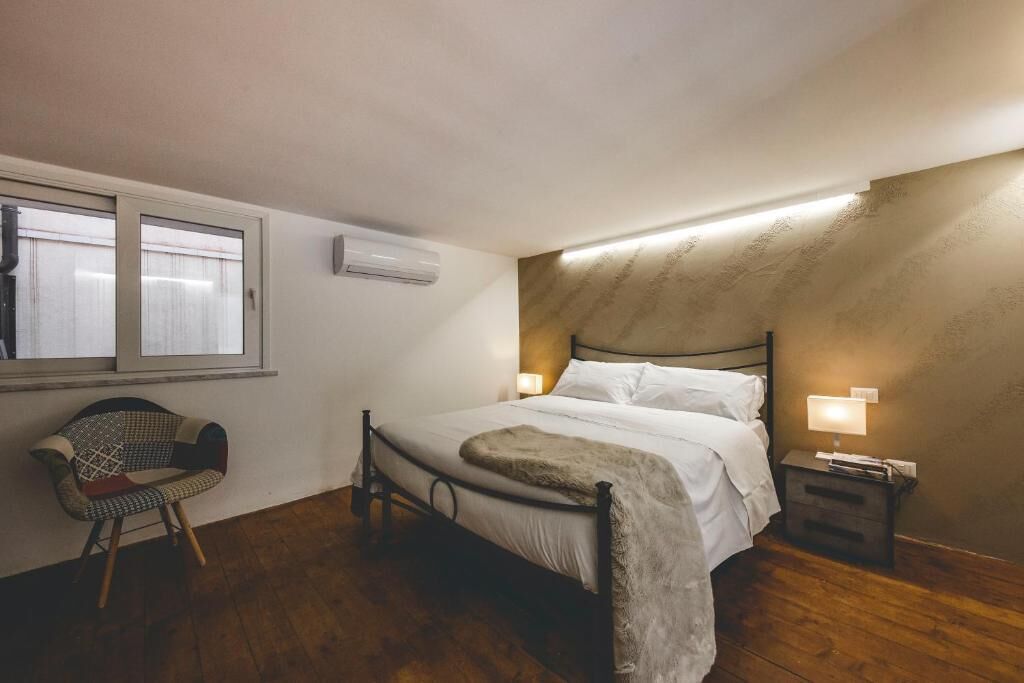 Um quarto com uma cama, luminárias de cabeceira, uma cadeira e uma janela.