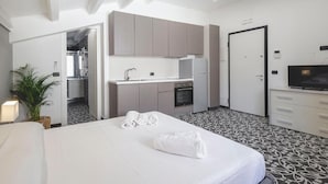 A hotel room with a bed, a small kitchenette, a TV, and a bathroom visible through an open door. - Pietranera Home (Catania)