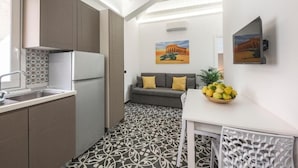 A compact kitchen with modern appliances, a dining area with a white table and chairs, and a sofa with yellow cushions. - Pietranera Home (Catania)