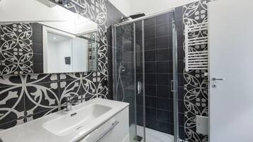 A modern bathroom with a double sink, a glass shower enclosure, and decorative black and white tiles.