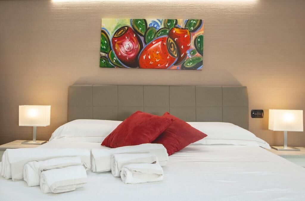 A hotel room with a neatly made bed, two bedside lamps, and a colorful painting on the wall.