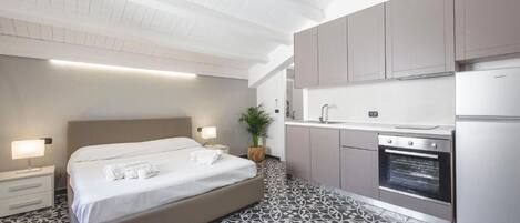 A modern hotel room with a large bed, bedside lamps, a built-in oven, and a kitchenette.