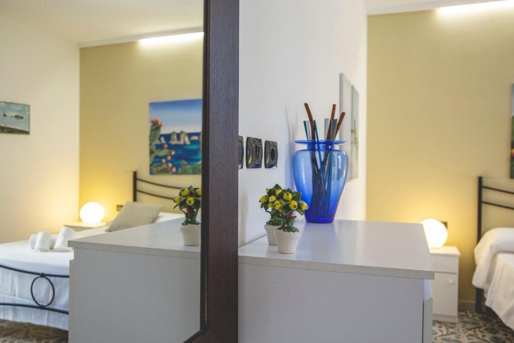 Una habitación de hotel con una cama, una mesita de noche y un escritorio pequeño con un florero y plantas.