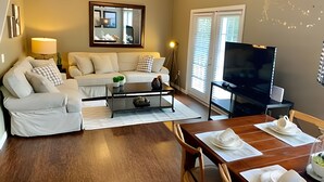 Ein Wohnzimmer mit Sofa, Couchtisch, Fernseher und Esstisch für zwei Personen.