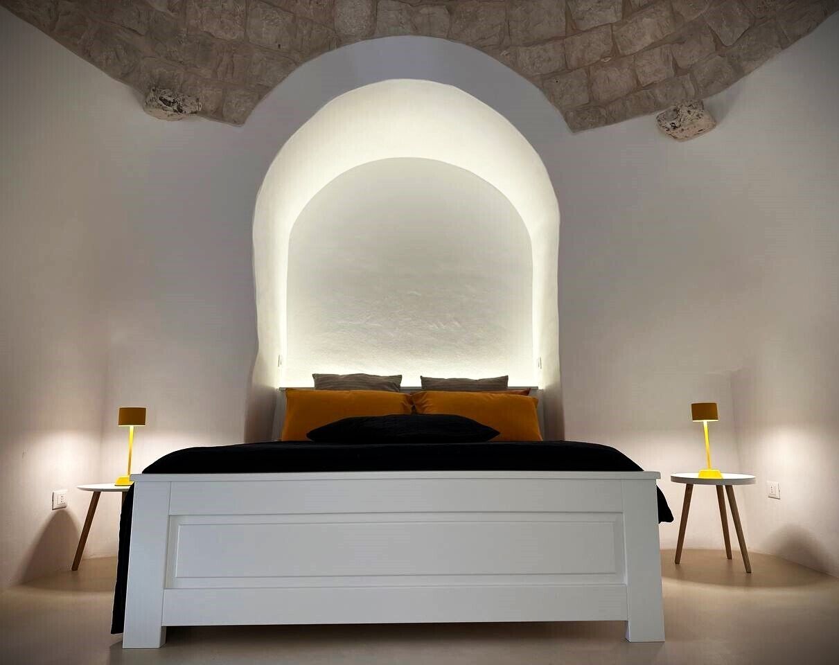 A bedroom with a white bed, a stone archway, and two bedside tables with lamps.
