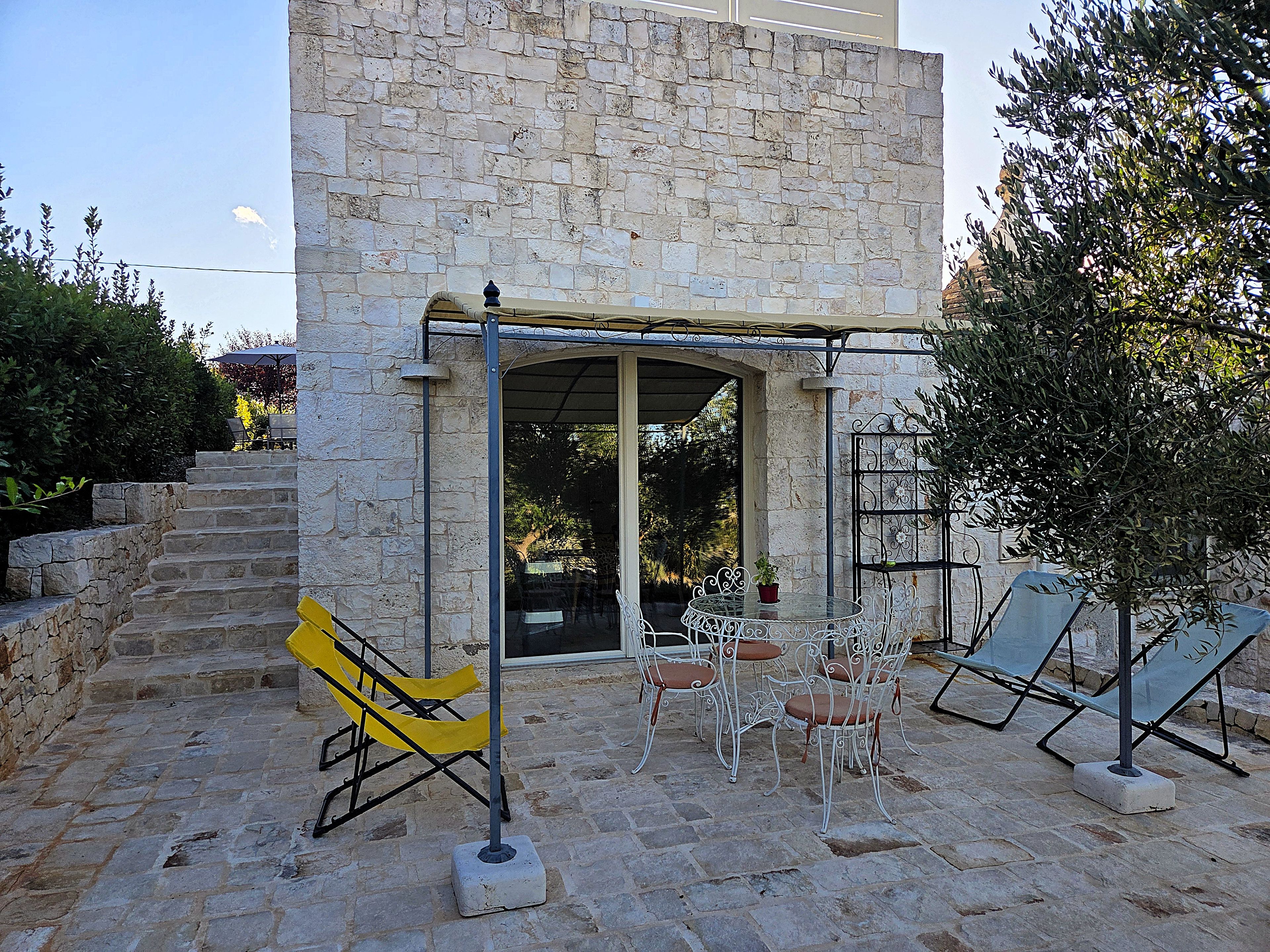A stone building with a covered patio area featuring outdoor seating and a staircase leading to an upper level.