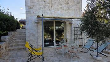 A stone building with a covered patio area featuring outdoor seating and a staircase leading to an upper level.