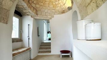A narrow hallway with a stone ceiling, a staircase, and a white shelf with kitchenware.